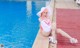 A woman in a pink bikini and white hat sitting by a pool.