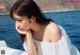 A woman in a white dress sitting on a boat by the water.