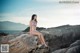 A woman in a bikini sitting on a rock by the ocean.