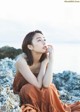 A woman sitting on a rock by the ocean.